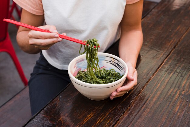 Close-up of a woman's hand eating green seaweed with red chopsticks