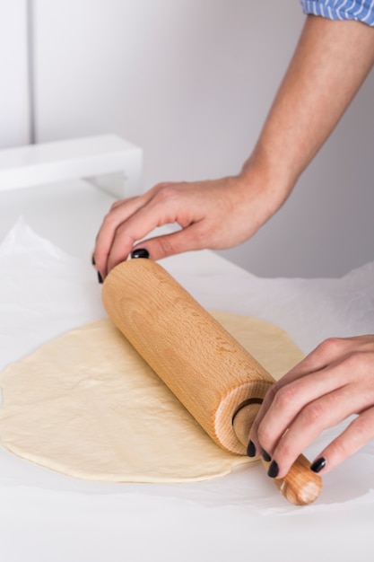 Close-up of a woman's hand flattening the dough with rolling pin on parchment paper