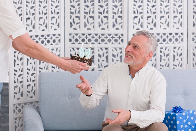 Close-up of woman's hand giving birthday cake to her smiling husband