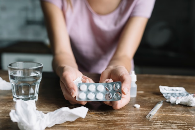 Primo piano della mano di una donna che tiene blister con le medicine sullo scrittorio di legno