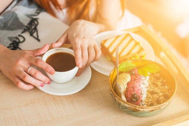 Close-up of woman's hand holding bowl of oatmeal with fruits on tray