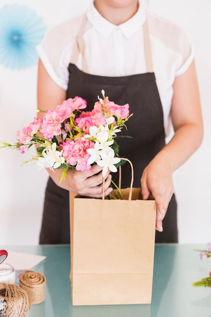 Close-up of a woman's hand holding flowers with paper bag on desk