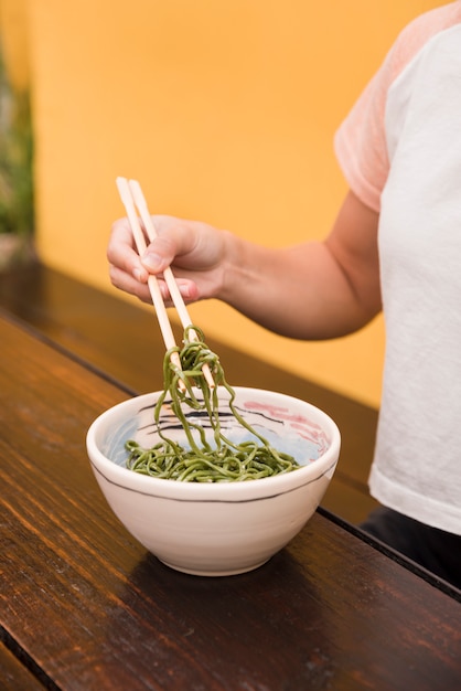 Close-up of woman's hand holding green seaweed salad with chopstick on wooden table