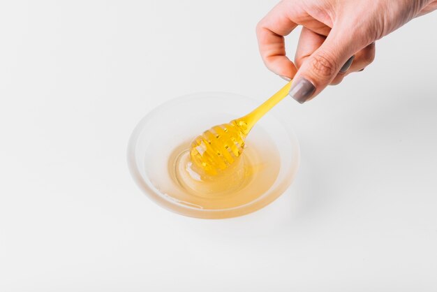 Close-up of a woman's hand holding honey dipper on white background
