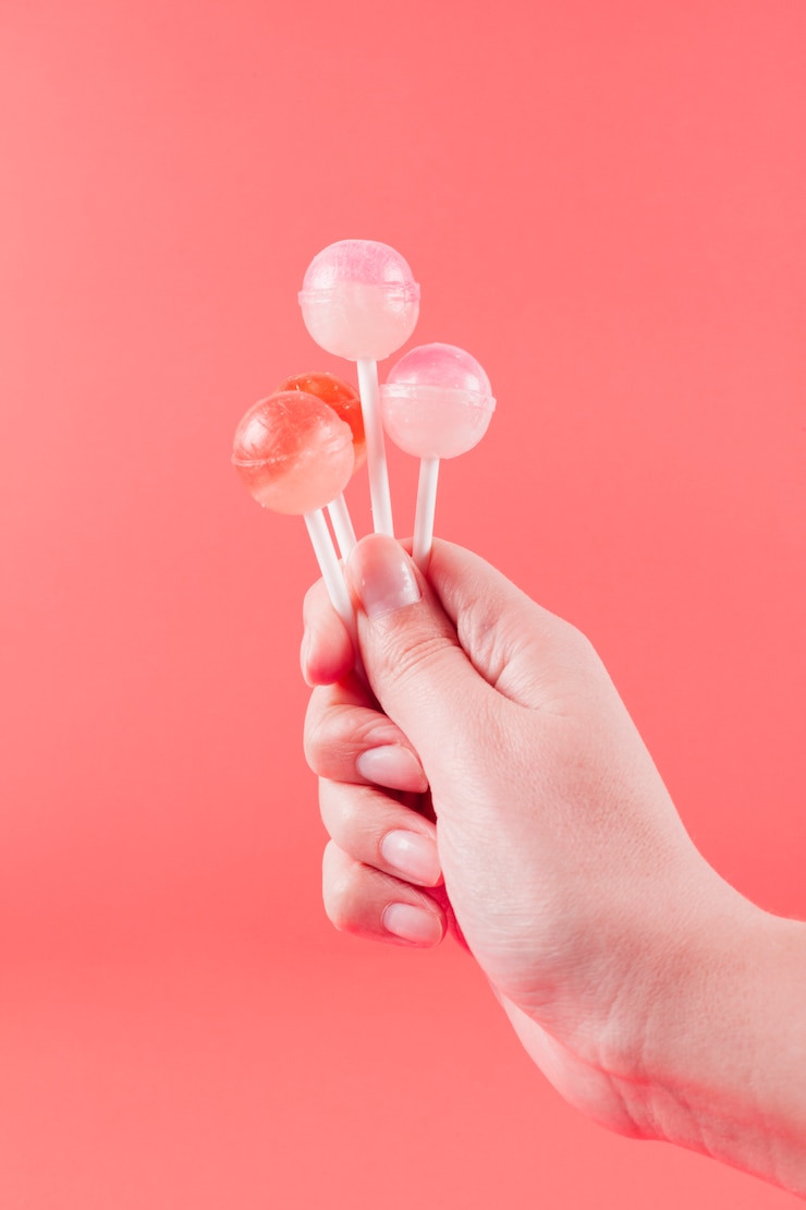 Free Photo close-up of woman's hand holding lollipops against coral backdrop