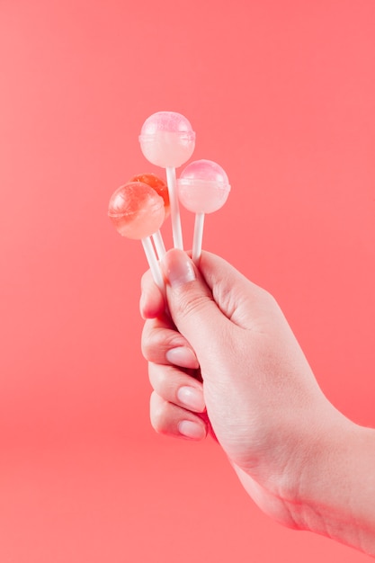 Close-up of woman's hand holding lollipops against coral backdrop