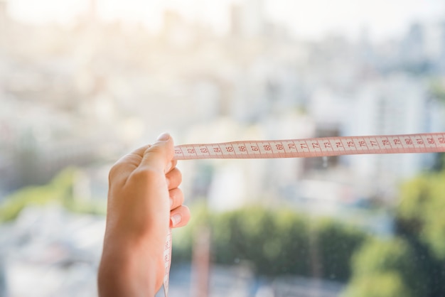 Close-up of woman's hand holding measuring tape against blurred backdrop