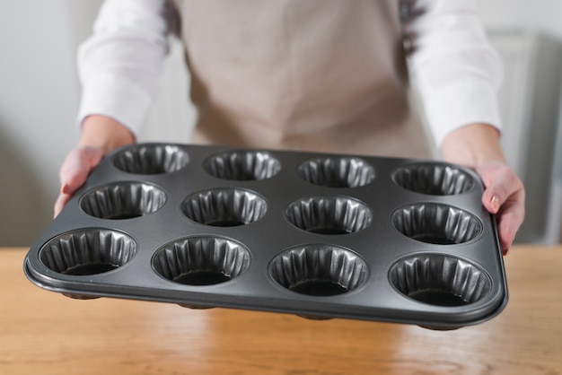 Primo piano della vaschetta del vassoio del bigné del muffin del metallo della tenuta della mano della donna