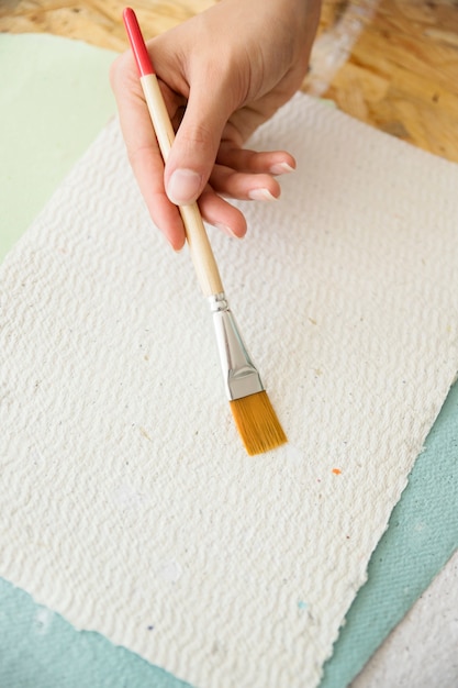 Close-up of a woman's hand holding paintbrush over white paper