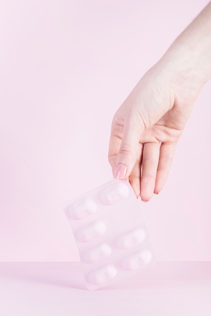 Free photo close-up of a woman's hand holding pink blister against pink background