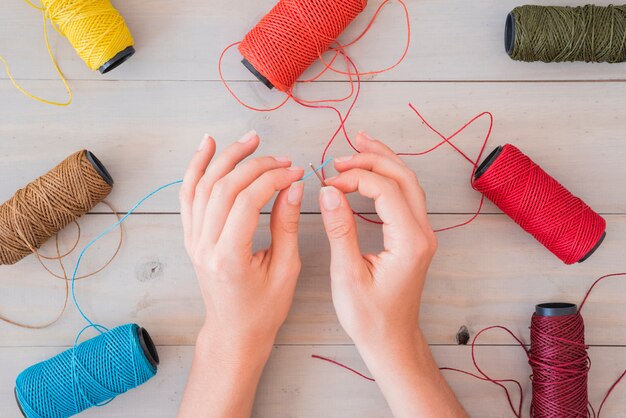 Close-up of a woman's hand inserting blue yarn in needle on wooden table