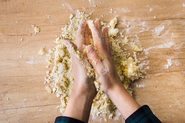 Конец-вверх руки женщины замешивая тесто для готовить итальянские клецки на деревянном столе