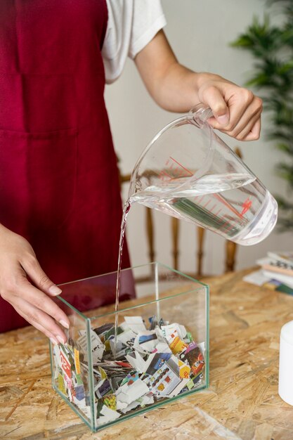 Close-up of a woman's hand pouring water on torned paper in container