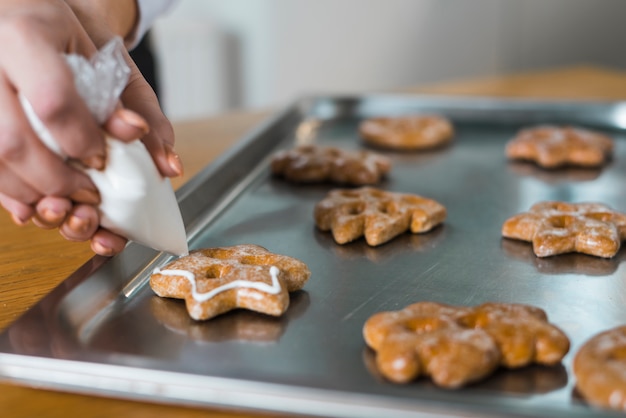 Close-up of woman's hand squeezing cream on traditional christmas cookie over the baking tray