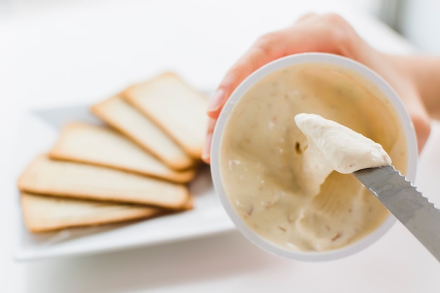 Close-up of a woman's hand taking the creamy cheese spread with knife