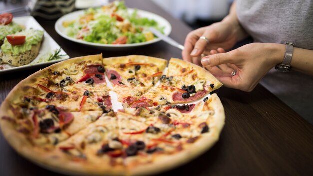 Close-up of a woman's hand taking slice of pepperoni pizza from plate