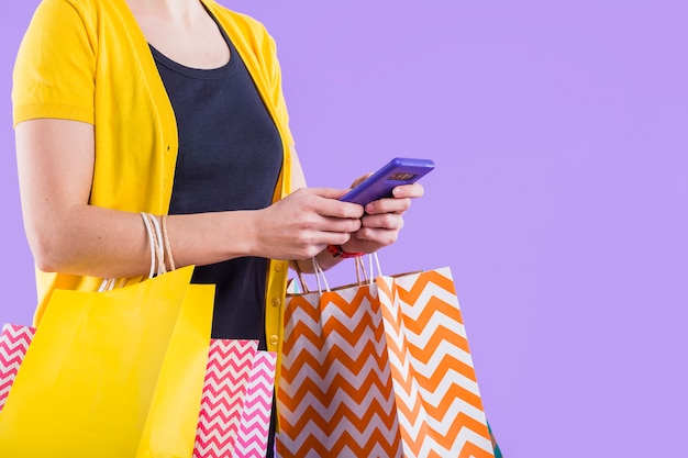 Close-up of woman's hand using cellphone white carrying shopping bag