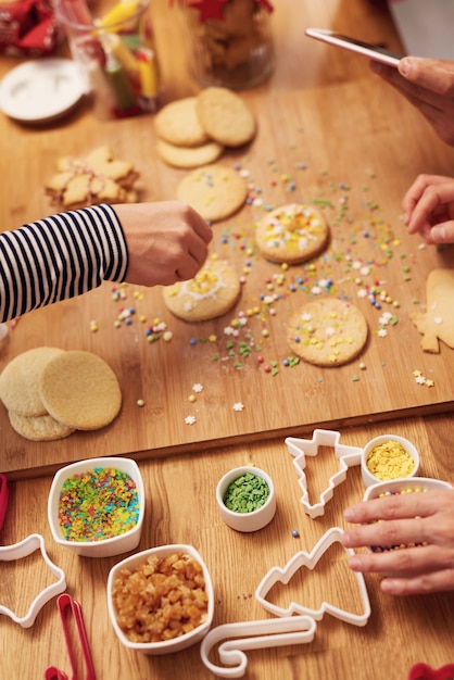 Chiuda in su delle mani della donna che decorano i biscotti per natale