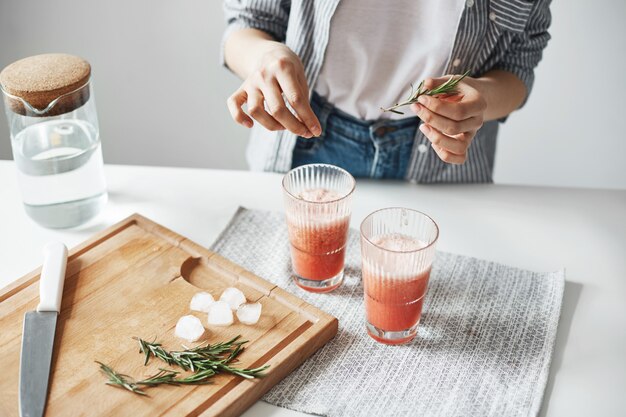 Close up of woman's hands decorating grapefruit detox healthy smoothie with rosemary.