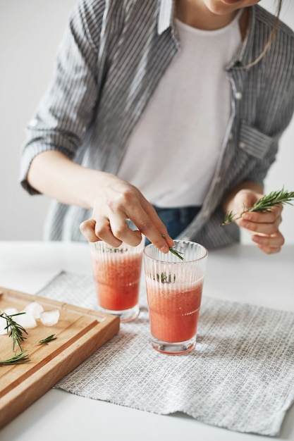 Закройте вверх рук женщины украшая smoothie детоксикации грейпфрута здоровый с розмариновым маслом.