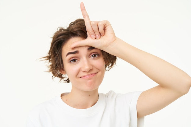 Free photo close up of woman shows loser gesture l letter on forehead and smiling mocking makes fun of someone