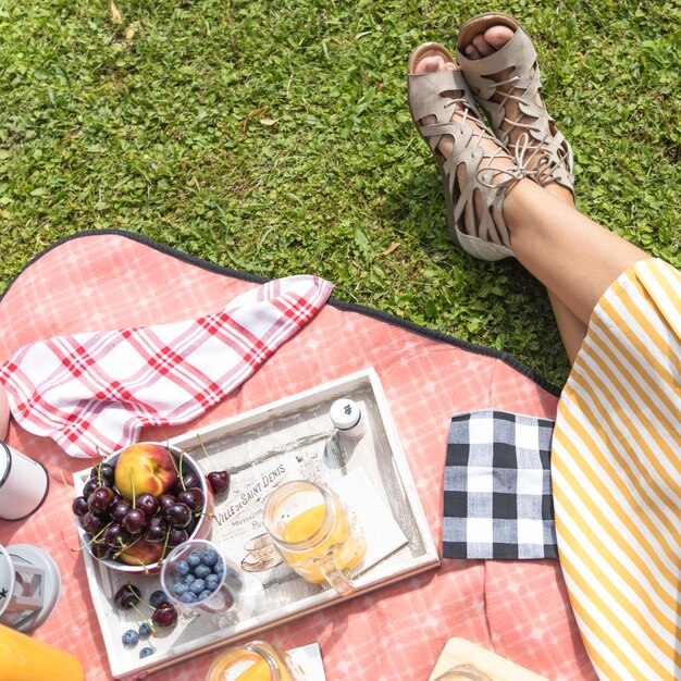 Close-up of woman sitting on blanket with fruits and juice in tray