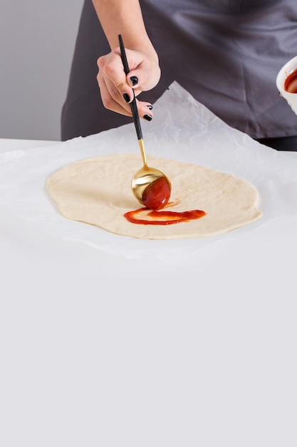 Close-up of a woman spreading the tomato sauce on pizza bread over the parchment paper