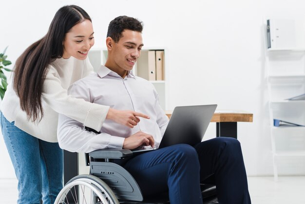 Close-up of a woman standing behind the businessman sitting on wheelchair showing something on laptop