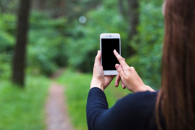 携帯電話の画面を使用して森に立っている女性のクローズアップ