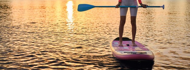 Close up of woman standing on sup board with paddle