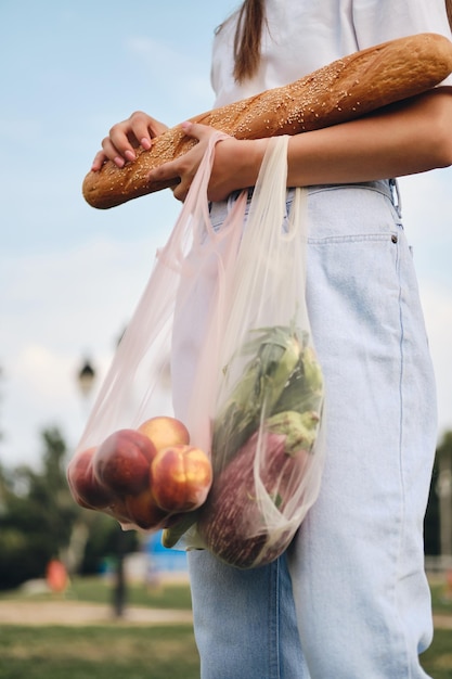 無料写真 都市公園のエコバッグにバゲットのパン桃と野菜と一緒に立っている女性をクローズアップ