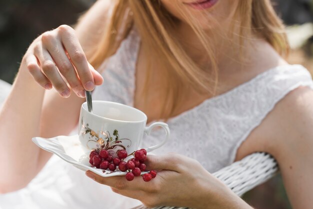 セラミックカップのスプーンでコーヒーをかき混ぜる女性のクローズアップ