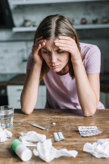 Close-up of a woman suffering from fever with medicines and crumpled tissue paper on wooden desk