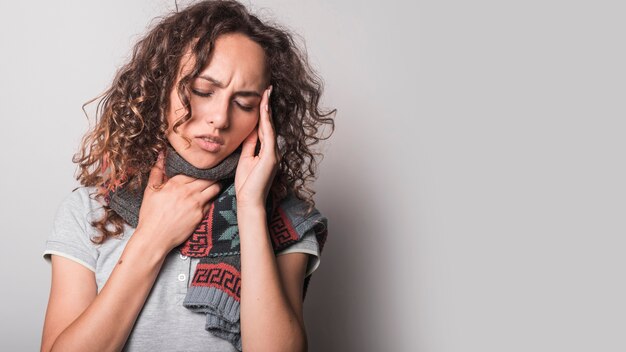 Close-up of woman suffering from flu having headache against gray background