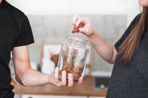 Close-up of woman taking crunchy cookies from glass jar hold by a man