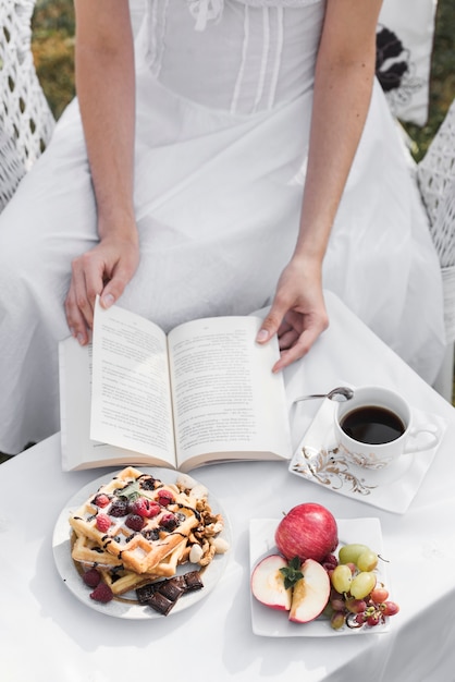 朝食とコーヒーテーブルの上の本のページをめくる女性のクローズアップ
