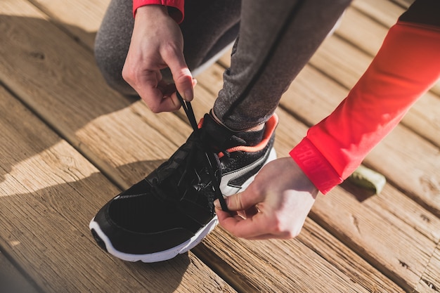 Close-up of woman tying her shoelaces on wooden floor