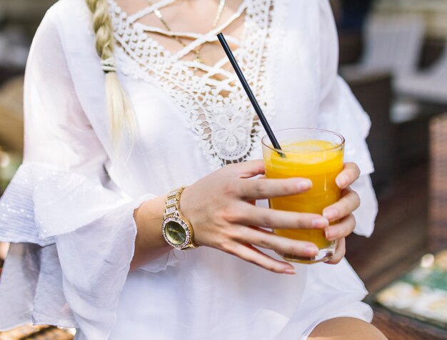 Close-up of a woman in white dress holding glass of healthy juice