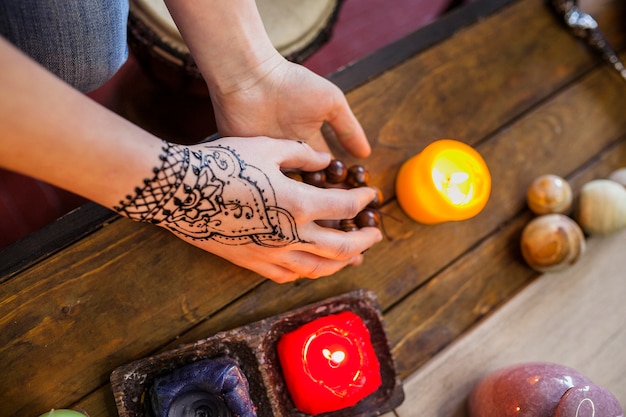 Close-up of woman with arabic mehndi on her hand holding beads on wooden desk