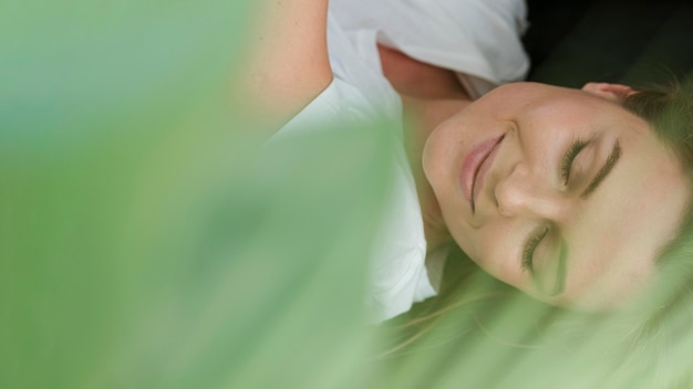 Close-up woman with closed eyes and blurred plant