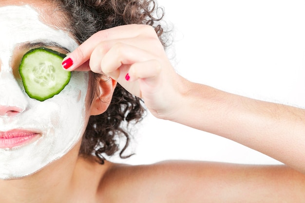 Free photo close-up of woman with deep cleansing nourishing face mask holding cucumber over eyes