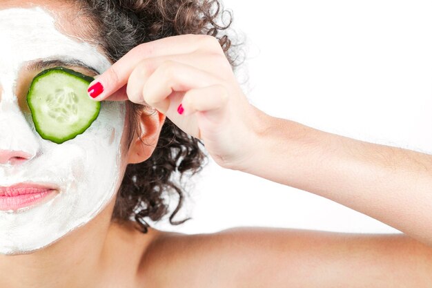 Close-up of woman with deep cleansing nourishing face mask holding cucumber over eyes