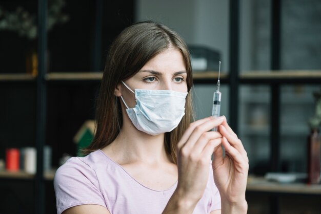 Close-up of a woman with protective mask holding syringe