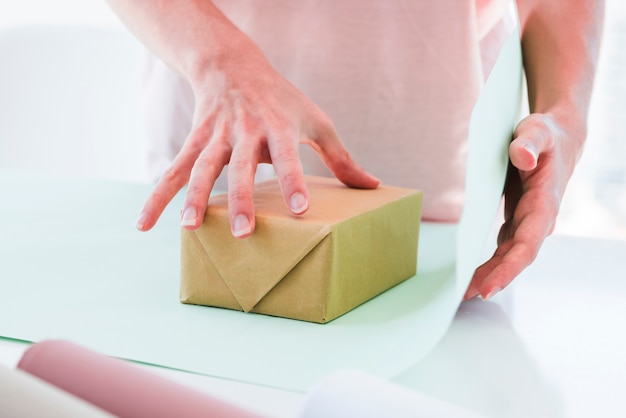 Close-up of woman wrapping the gift box with paper on table