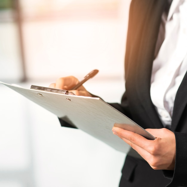 Free Photo close-up of a woman writing on clipboard with pen