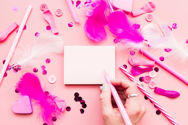 Close-up of woman writing the notepad with pen and decorative items on pink background