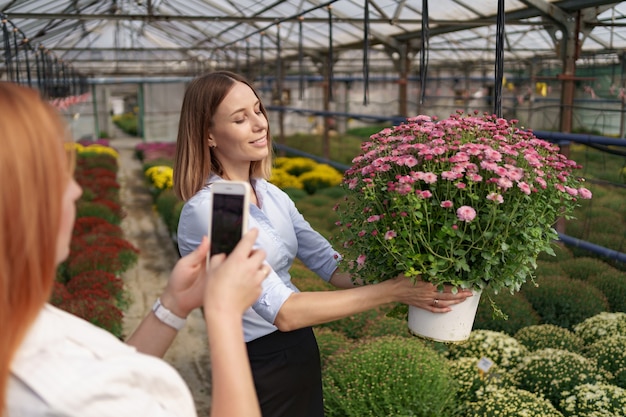 電話を持って、花を持つ少女の写真を撮る女性の手を閉じます。