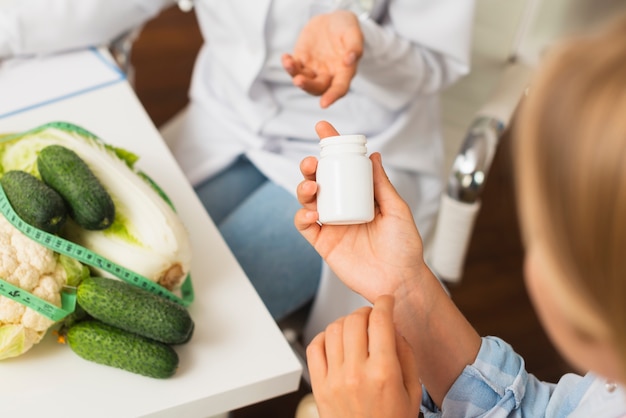 Close-up women with vegetables and pill container