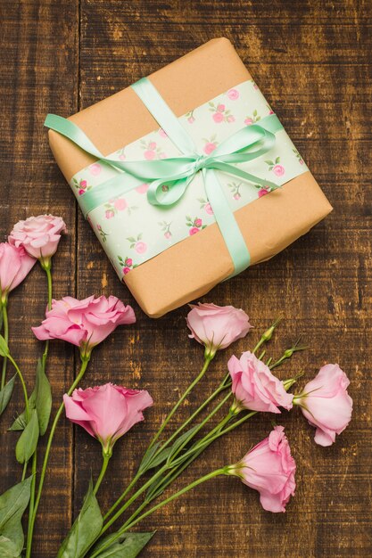 Крупный план обернутой посылки и розовый свежий цветок на столе