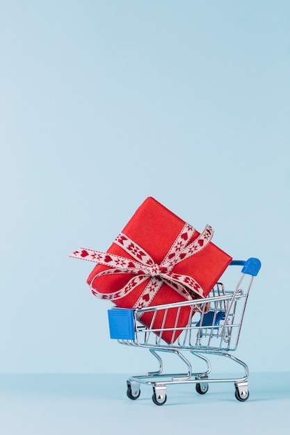 Free photo close-up of wrapped red gift box in shopping cart on blue backdrop